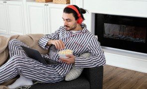homem de pijamas longos sentado no sofá comendo pipoca