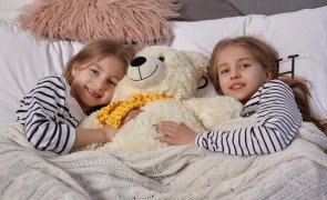 duas meninas deitadas na cama abracando um urso de pelucia
